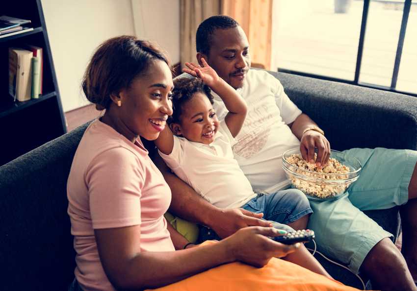 Black family eating popcorn while watching movie at home