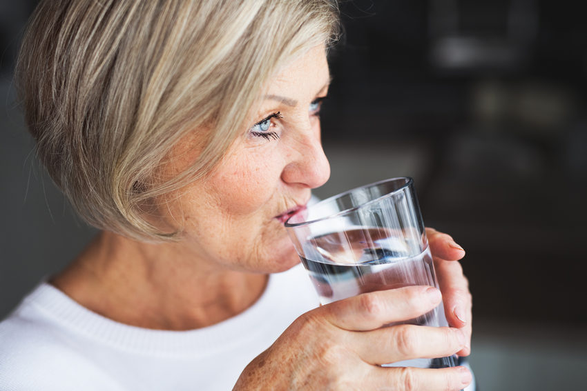 Senior woman drinking water in the kitchen.