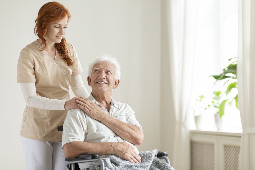 Smiling elderly man in a wheelchair and friendly caregiver in a