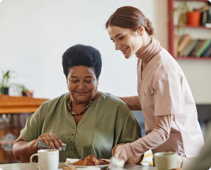 A caregiver assists an elderly woman with breakfast, showcasing compassion and support in senior care.