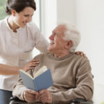 Photo of elderly man reading book and his personal home assistence Personal care homes in Philadelphia
