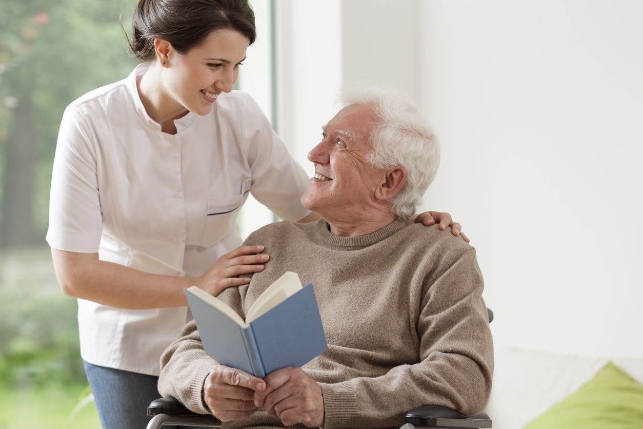 Photo of elderly man reading book and his personal home assistence Personal care homes in Philadelphia