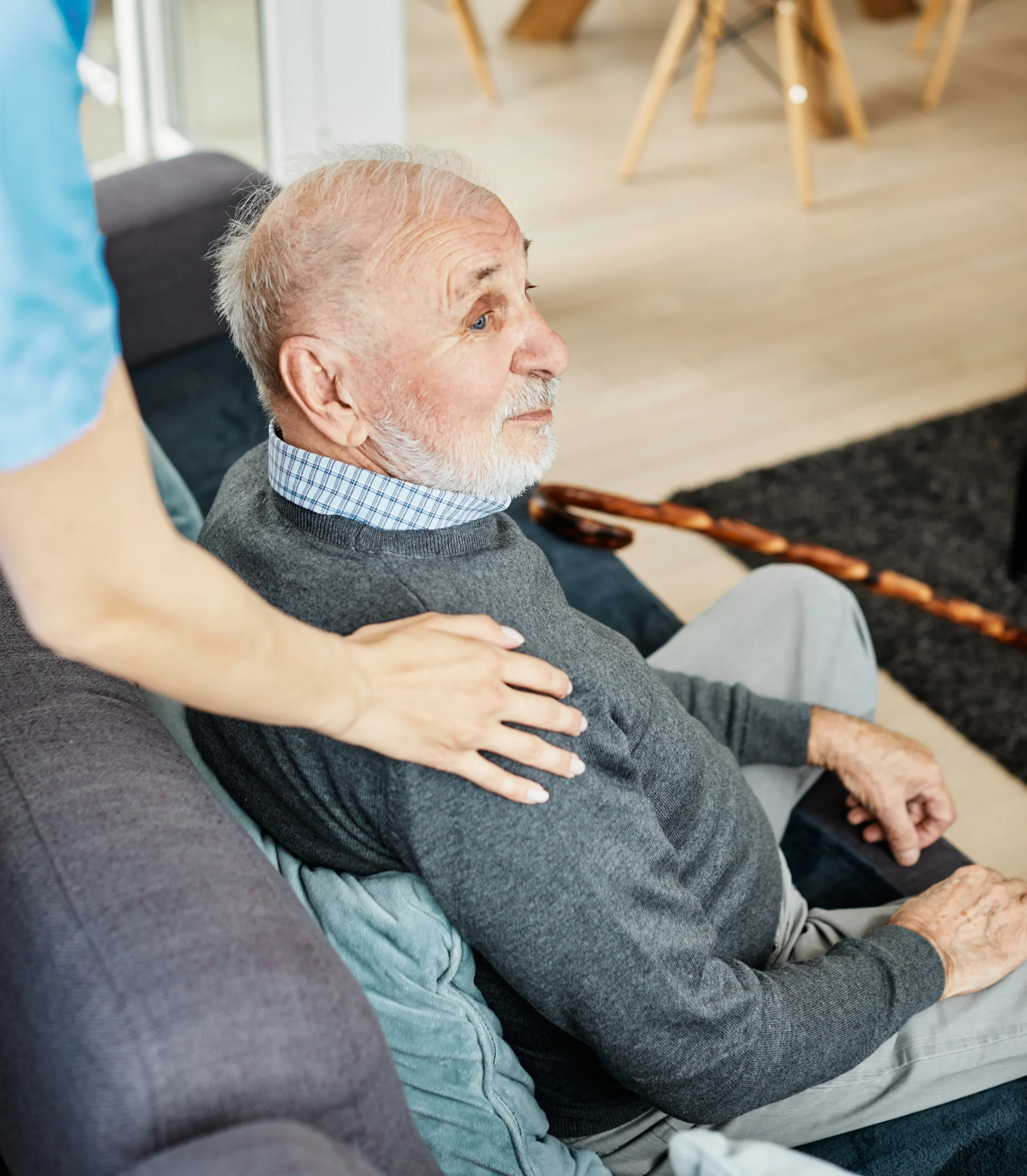 Elderly man in chair with caregiver's hand on shoulder