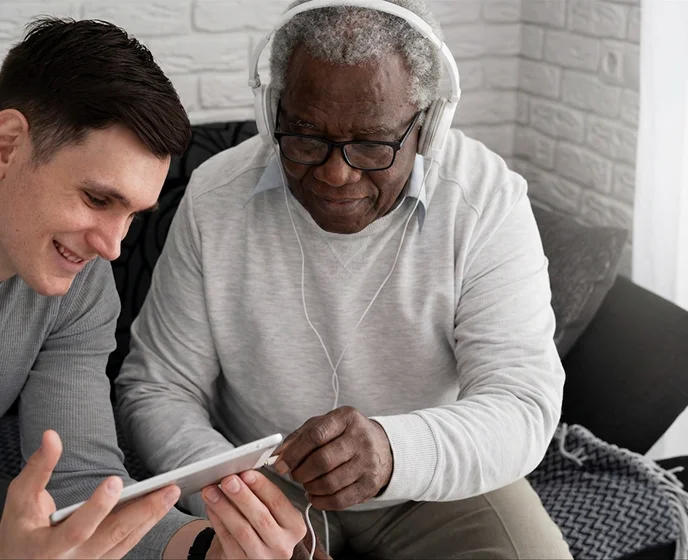 Caregiver helping senior man use tablet technology and digital communication at home