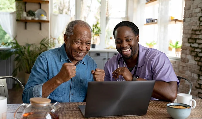 Caregiver helping senior man use laptop and technology during home care assistance