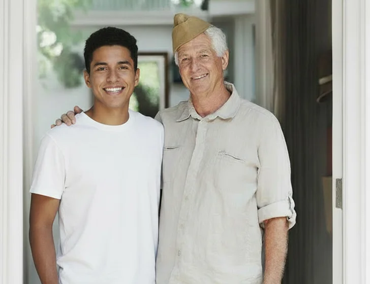 Young man and senior father standing together in home doorway