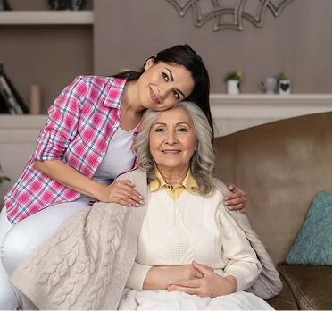 Caring daughter embracing senior mother on cozy living room couch