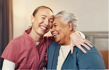 Compassionate nurse hugging smiling senior woman during care visit