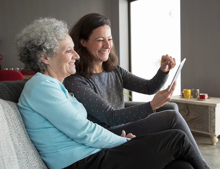 Senior woman and caregiver using tablet for video calls and digital companionship at home