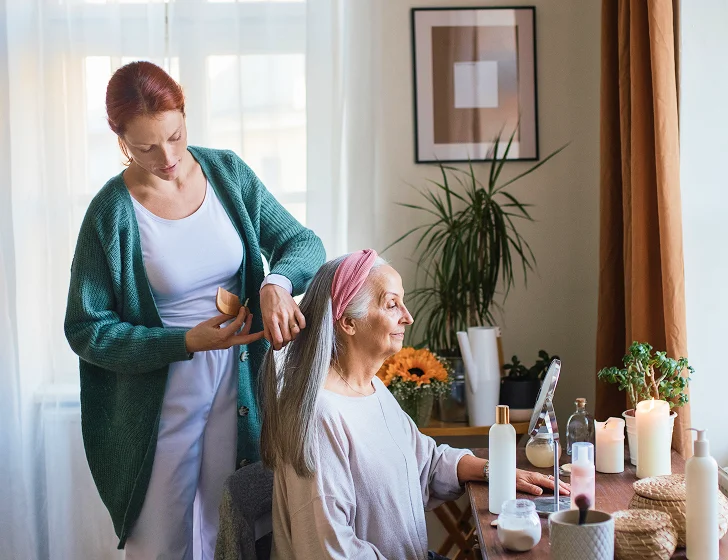 Caregiver helping senior woman with hair care and personal grooming at home