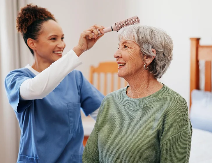 Caregiver assisting senior woman with hair brushing and personal grooming services at home