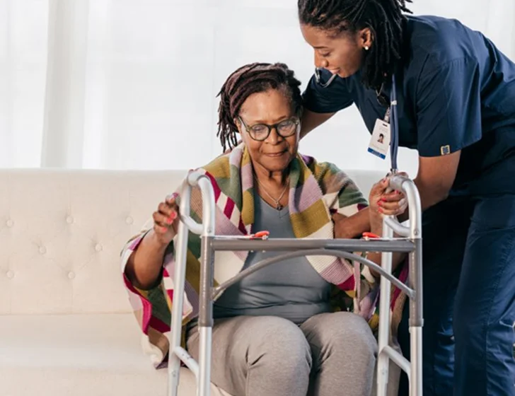 Professional caregiver assisting senior woman with walker during rehabilitation support