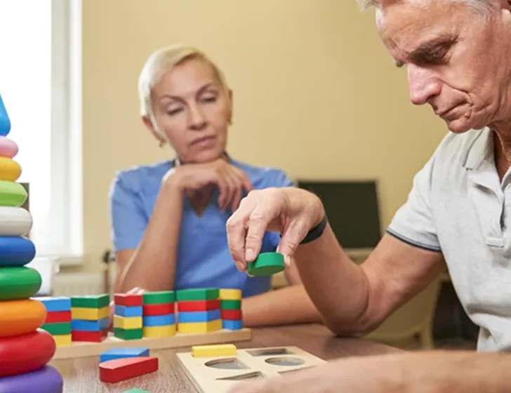 Senior man participating in cognitive therapy activity with caregiver assistance