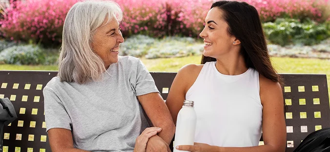 Caregiver and senior woman enjoying conversation outdoors on a park bench