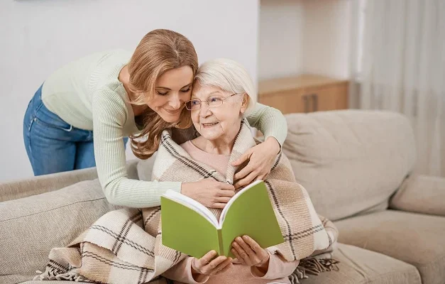 Caregiver reading with senior woman on a living room sofa