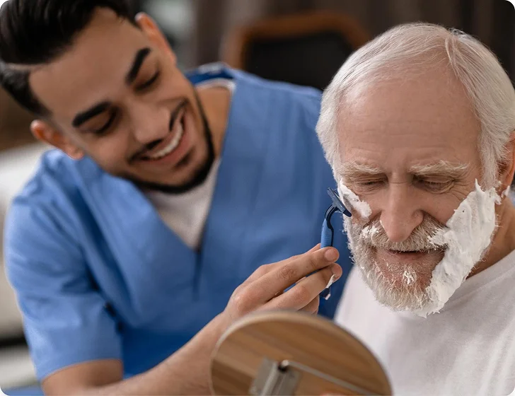 Caregiver assisting senior man with personal grooming and shaving