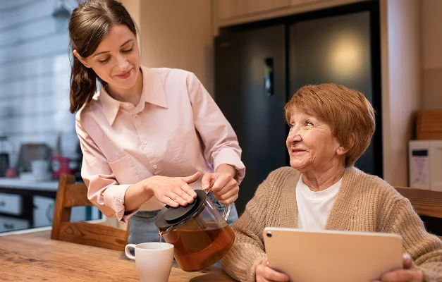 Young woman pours tea for an older woman using a tablet