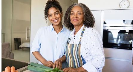 Two women, a younger Black woman and an older Black woman, smile in a kitchen.